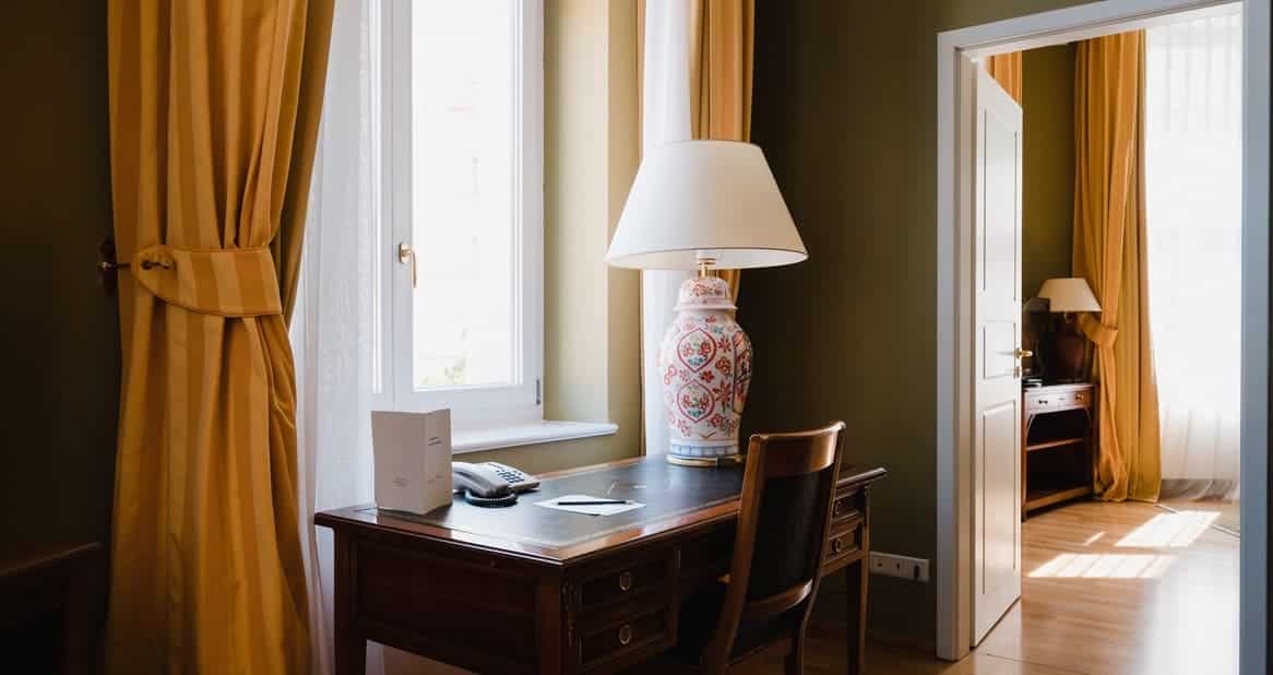 Schreibtisch mit handbemalter Lampe und Telefon im Louisa´s Place Hotel. Die Sonne scheint durch die Fenster. Recht mit Blick ins Schlafzimmer.