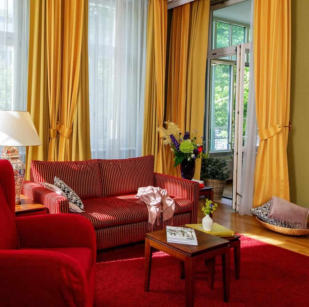 Wohnbereich Ansicht mit rotem Sofa und gelben Vorhängen der Grandsuite des Louisa's Place Hotel am Kudamm Berlin